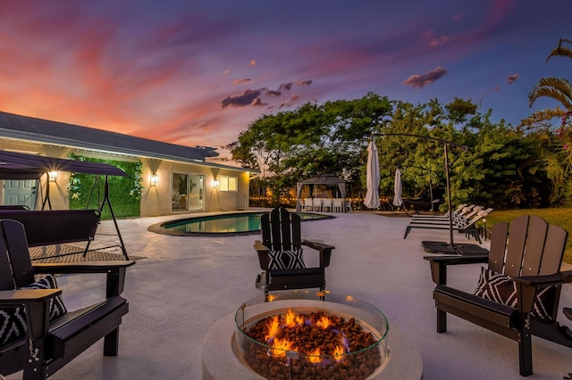 pool at dusk featuring an outdoor fire pit, a gazebo, and a patio area