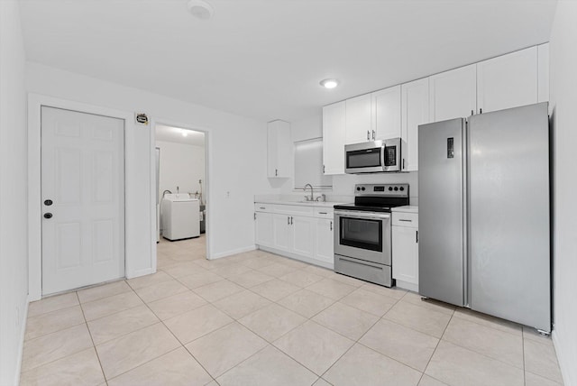 kitchen with washer / dryer, appliances with stainless steel finishes, white cabinets, sink, and light tile patterned flooring