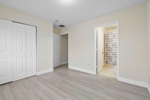 unfurnished bedroom with a closet, ensuite bath, and light hardwood / wood-style flooring