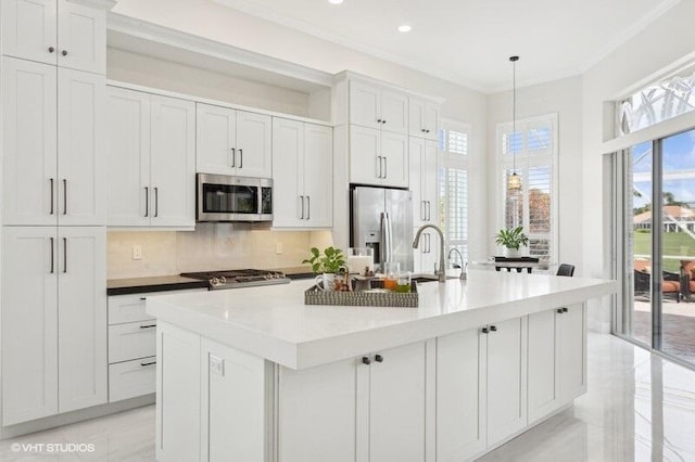 kitchen with hanging light fixtures, an island with sink, white cabinets, and appliances with stainless steel finishes