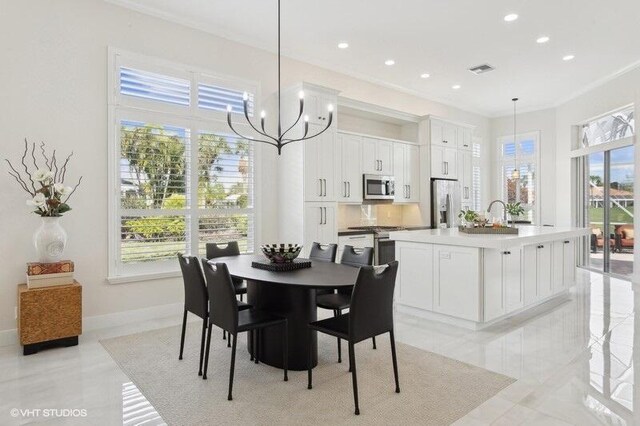 kitchen with sink, appliances with stainless steel finishes, hanging light fixtures, an island with sink, and white cabinets