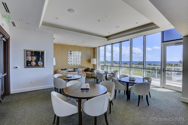 dining space featuring dark carpet, a wall of windows, and a raised ceiling