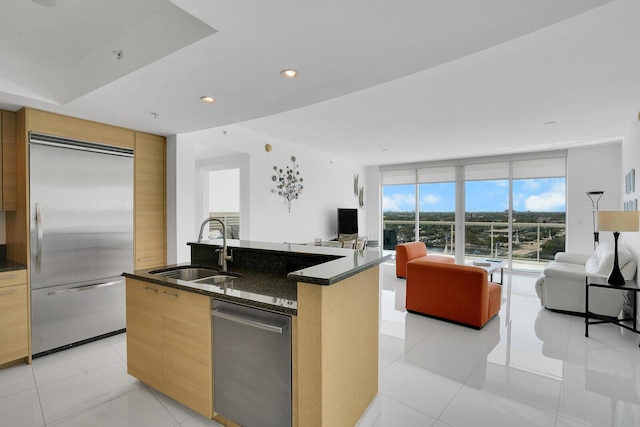 kitchen with sink, appliances with stainless steel finishes, a kitchen island with sink, dark stone countertops, and light tile patterned flooring