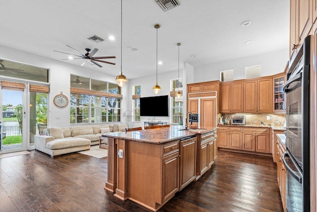 kitchen featuring pendant lighting, light stone counters, a kitchen island with sink, dark hardwood / wood-style floors, and decorative backsplash