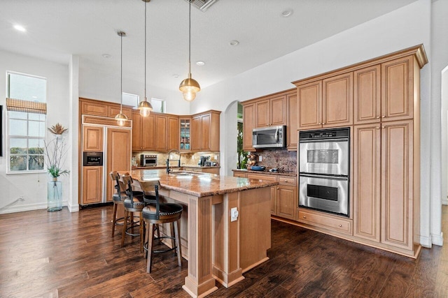 kitchen featuring appliances with stainless steel finishes, decorative light fixtures, sink, light stone counters, and a center island with sink