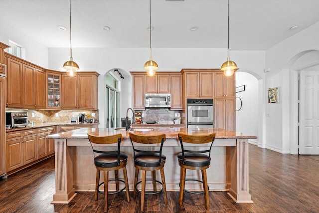 kitchen featuring a center island with sink, light stone counters, tasteful backsplash, and appliances with stainless steel finishes