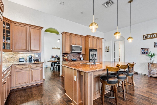 kitchen featuring an island with sink, hanging light fixtures, appliances with stainless steel finishes, and backsplash