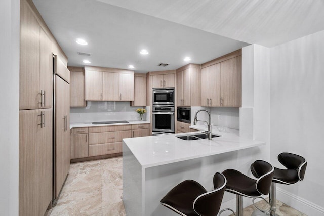 kitchen with sink, black appliances, light brown cabinetry, decorative backsplash, and kitchen peninsula