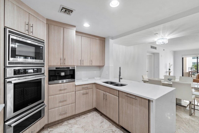 kitchen with light brown cabinetry, sink, an inviting chandelier, stainless steel microwave, and kitchen peninsula