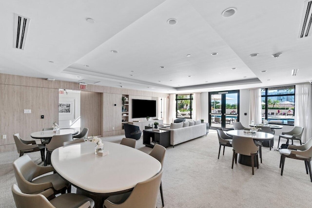 carpeted dining area featuring a tray ceiling, wooden walls, and french doors