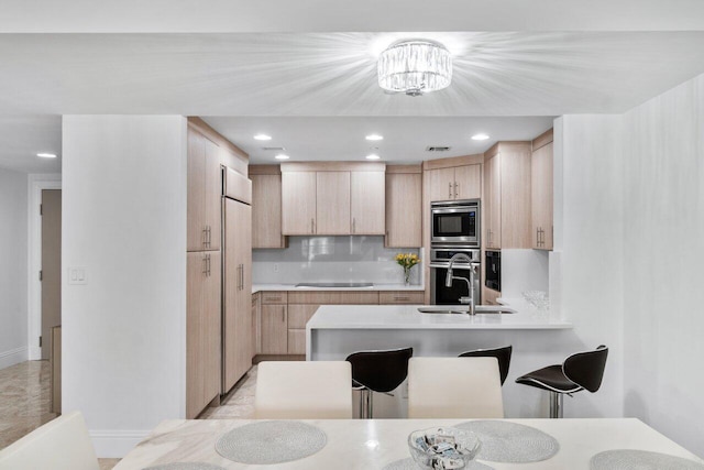 kitchen featuring light brown cabinetry, sink, decorative backsplash, built in appliances, and a notable chandelier