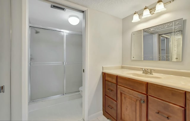 bathroom featuring toilet, vanity, a textured ceiling, and a shower with shower door