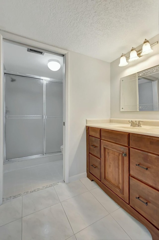 bathroom with tile patterned flooring, vanity, an enclosed shower, and a textured ceiling