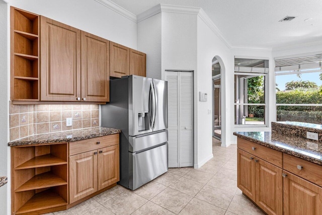 kitchen with light tile patterned flooring, stainless steel fridge with ice dispenser, dark stone countertops, ornamental molding, and decorative backsplash