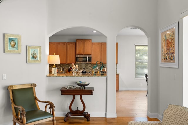 kitchen featuring light stone countertops, light wood-type flooring, and tasteful backsplash