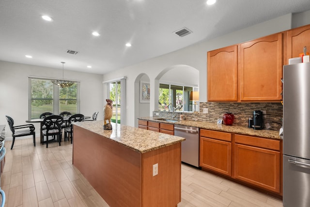 kitchen with a center island, appliances with stainless steel finishes, hanging light fixtures, sink, and light stone counters