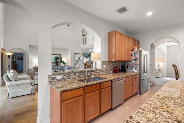 kitchen featuring light stone countertops, stainless steel appliances, decorative backsplash, sink, and light wood-type flooring