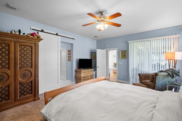 carpeted bedroom with ceiling fan, a barn door, and a textured ceiling