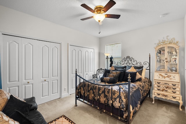 carpeted bedroom featuring multiple closets, ceiling fan, and a textured ceiling