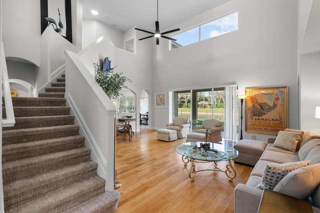 living room with ceiling fan, wood-type flooring, and a towering ceiling