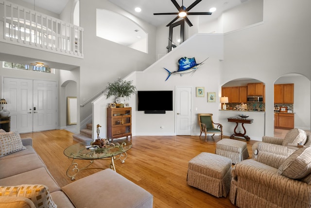 living room with light wood-type flooring, a towering ceiling, and ceiling fan