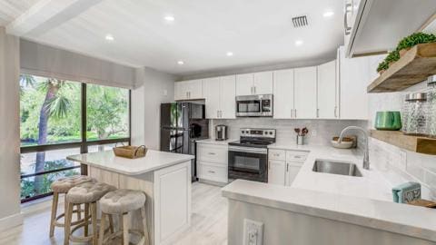 kitchen featuring a kitchen bar, white cabinetry, stainless steel appliances, decorative backsplash, and sink