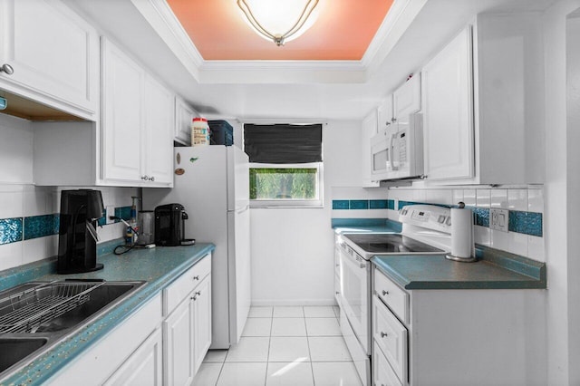 kitchen with white appliances, white cabinets, ornamental molding, light tile patterned floors, and a tray ceiling