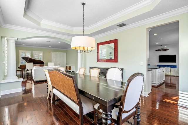 dining area with crown molding, dark wood-type flooring, ornate columns, and a raised ceiling