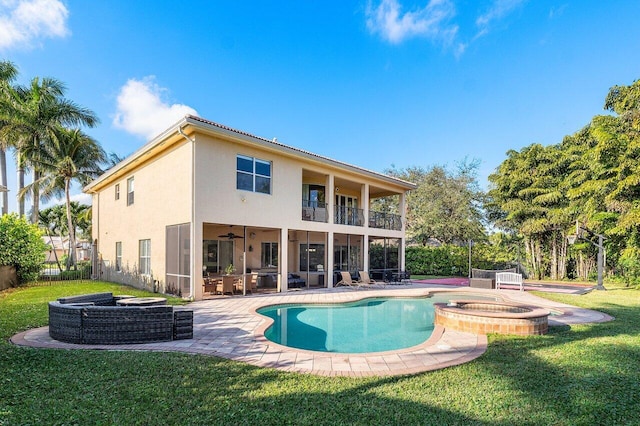 back of house with a balcony, a patio area, ceiling fan, a pool with hot tub, and a lawn