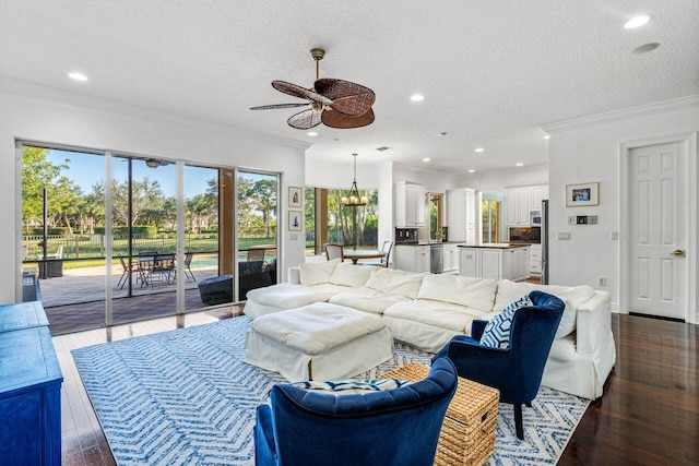 living room featuring ceiling fan with notable chandelier, dark hardwood / wood-style flooring, crown molding, and a textured ceiling