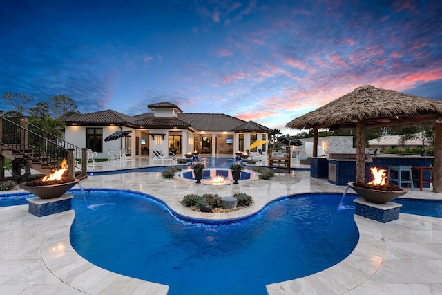 pool at dusk with a fire pit, a patio area, and pool water feature