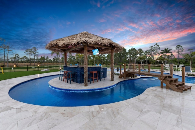 pool at dusk with a patio and an outdoor bar