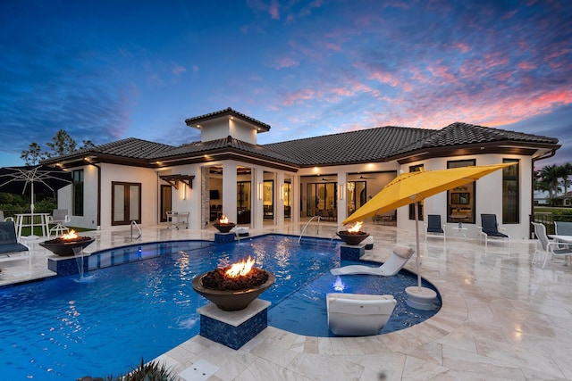 pool at dusk featuring a patio, pool water feature, ceiling fan, and a fire pit