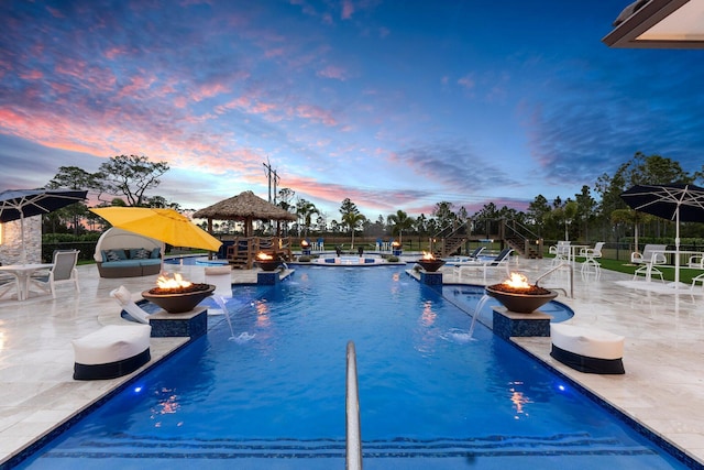 pool at dusk with a fire pit, pool water feature, and a gazebo