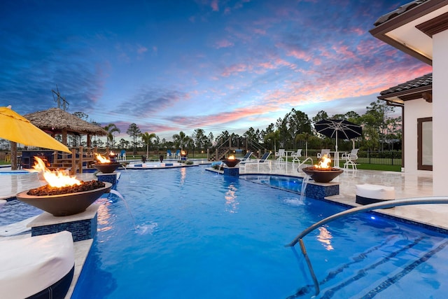 pool at dusk with a fire pit, pool water feature, and a gazebo