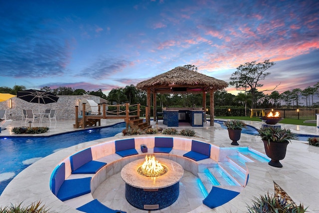 pool at dusk with a gazebo, an outdoor fire pit, and a patio