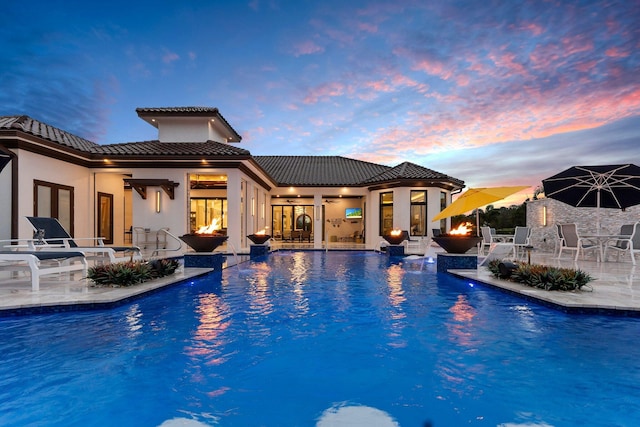 pool at dusk with a patio and ceiling fan