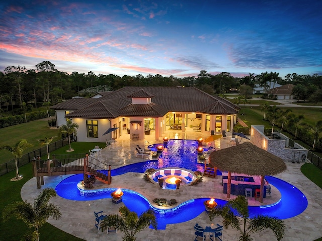 pool at dusk with an in ground hot tub and a patio area