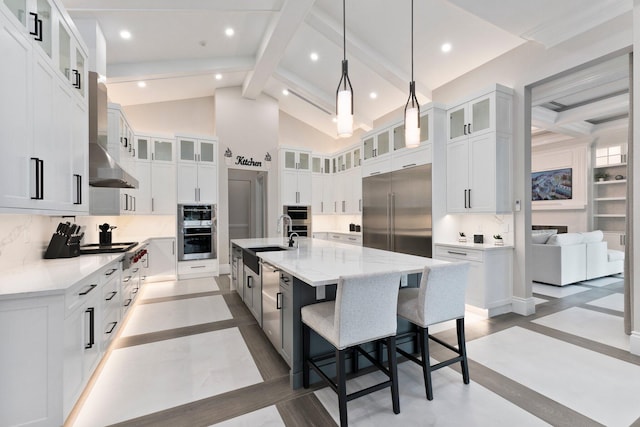 kitchen with appliances with stainless steel finishes, beam ceiling, a kitchen island with sink, decorative backsplash, and white cabinets