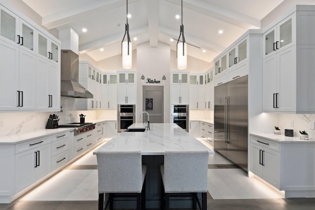 kitchen with appliances with stainless steel finishes, white cabinets, backsplash, wall chimney range hood, and a spacious island