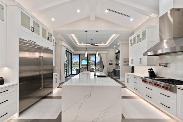 kitchen featuring wall chimney exhaust hood, white cabinetry, appliances with stainless steel finishes, and a center island with sink