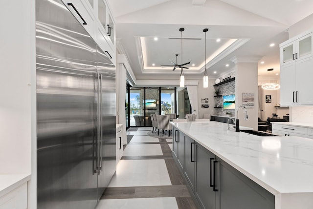 kitchen featuring stainless steel built in refrigerator, sink, decorative light fixtures, a tray ceiling, and white cabinets