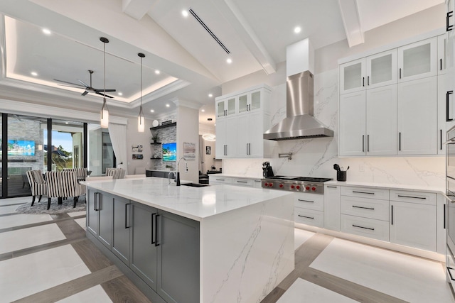 kitchen with a spacious island, sink, stainless steel gas cooktop, white cabinetry, and wall chimney range hood