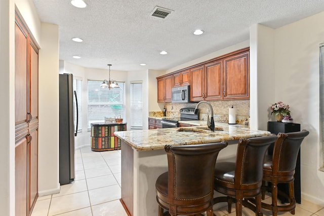 kitchen featuring sink, light tile patterned floors, stainless steel appliances, light stone counters, and kitchen peninsula