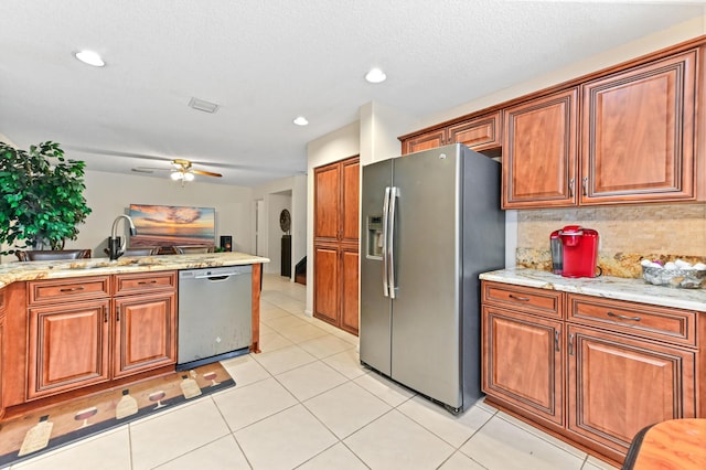 kitchen with light tile patterned floors, appliances with stainless steel finishes, ceiling fan, light stone countertops, and backsplash