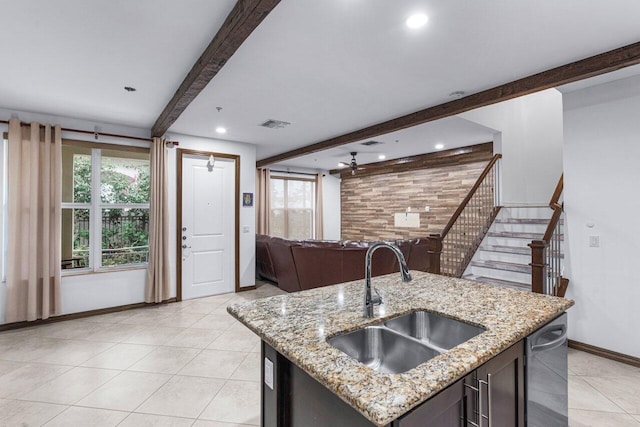 kitchen featuring sink, a kitchen island with sink, beam ceiling, and light stone countertops