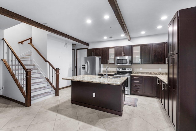 kitchen with appliances with stainless steel finishes, sink, a kitchen island with sink, light stone counters, and beam ceiling