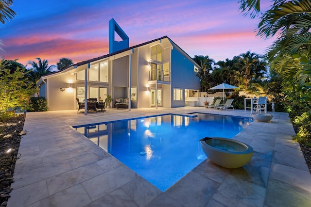 pool at dusk with a patio and an in ground hot tub