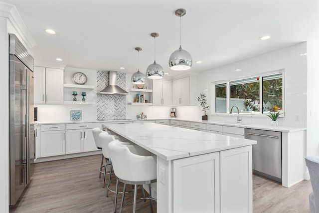 kitchen featuring appliances with stainless steel finishes, white cabinetry, sink, a kitchen island, and wall chimney exhaust hood