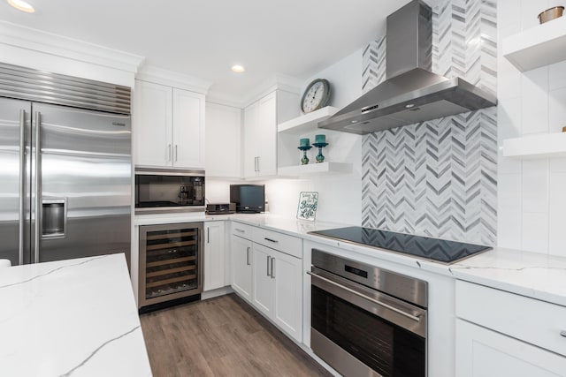 kitchen with beverage cooler, black appliances, wall chimney exhaust hood, white cabinetry, and light stone counters